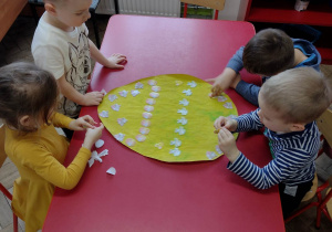 Dzieci ozdabiają żółtą pisankę naklejkami