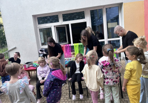 Dzieci siedzą na krzesełkach i mają zaplatane warkoczyki,