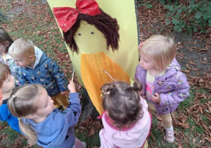 Dzieci ozdabiają papierową postać przedszkolaka przyklejoną do drzewa