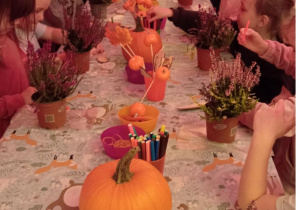 Dzieci siedzą przy stole i ozdabiają swoje wrzosy