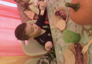 Dzieci siedzą przy stole i jedzą pieczone kiełbaski