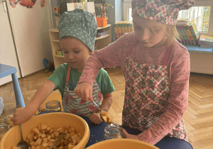 dzieci w kucharskich czapkach i fartuszku nakładają jabłka do słoików