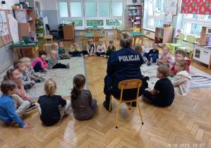 Dzieci siedza na dywanie i rozmawiają z Panią Policjantką
