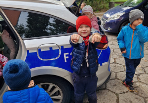 Dzieci ogladają radiowóz, a chłopiec pokazuje założone kajdanki na swoje ręce