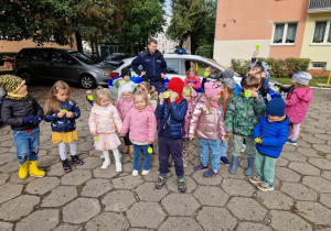 Dzieci stoją przed radiowozem razem z Panem Policjantem pokazując odblaski