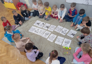 Dzieci siedzą na dywanie w kole, po środku rozłożone są karty pracy rozmawiają na temat Praw dziecka