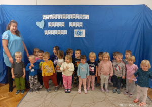 Zdjęcie grupowe najmłodszych pzredszkolaków z wychowawca gr Zajączki na tle niebieskim tle z białym napisem Międzynarodowy Dzień Praw Dziecka