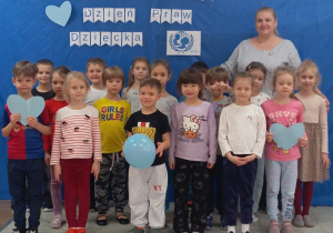 Zdjęcie grupowe najstarszych przedszkolaków z wychowawcą dzieci z grupy Sówki na tle niebieskim tle z białym napisem Międzynarodowy Dzień Praw Dziecka