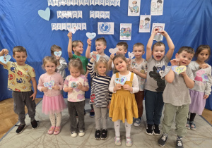 Dzieci z grupy Misiów stoją na tle niebieskim tle z białym napisem Międzynarodowy Dzień Praw Dziecka pokazując swoje narysowane serduszka