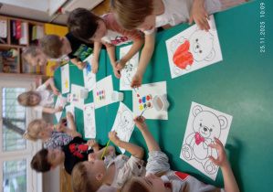 Dzieci przy stoliku malują farbami obrazek misia