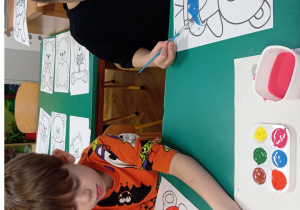 Chłopcy przy stoliku malują farbami obrazek misia