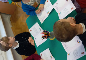 Dzieci siedzą przy stoliku i kolorują w swoich książkach.