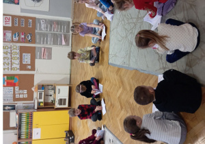 Dzieci siedza w kole na dywanie oglądając swoje książki i słuchając opowiadania.