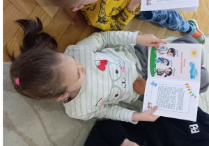 Dzieci leżą na podłodze trzymając swoją książkę.