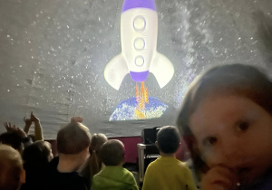 Dzieci siedzą na dywanie, oglądając start rakiety