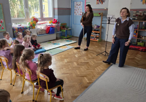 Dzieci siedzą na krzesełkach, słuchając jaki dzisiaj poznają instrument muzyczny.