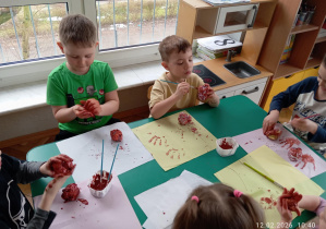 Dzieci malują brązową farbą pączki zrobione z papieru.