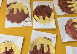 Na stole leżą prace plastyczne. Dzieci namalowały pączki z lukrem.