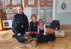 Hania i Tosia pod opieką Pani policjantki głaskają policyjnego psa Tadeusza.