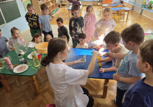Dzieci z zainteresowaniem przyglądają się eksperymentowi z balonem wykonywanemu przy stoliku.