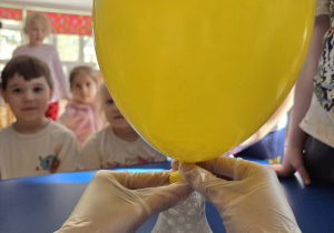 Balon napełnia się gazem podczas eksperymentu przeprowadzanego przez prowadzącą w rękawiczkach.