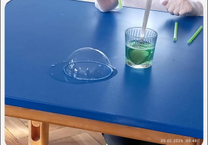 Na stole widoczna jest bańka mydlana oraz szklanka z kolorowym płynem używanym do eksperymentu.