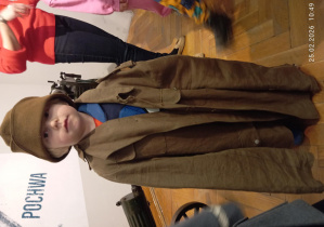 Chłopiec przebrany w wojskowy płaszcz i czapkę.