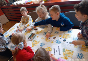 Dzieci przy stole dopasowują ilustracje przedstawiające przedmioty związane z żołnierzem.