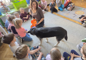 Dzieci siedzą w kręgu, i karmią pieska.