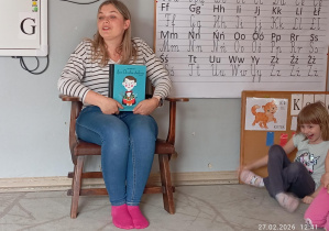 Pani Monika siedzi na fotelu i opowiada o książce, którą przyniosła przeczytać dzieciom.