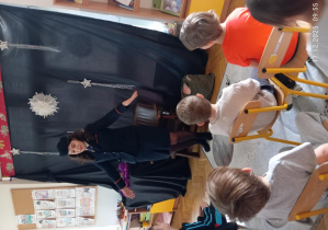 Dzieci siedzą na krzesełkach i słuchają jak Pani Monika opowiada o swojej pracy.