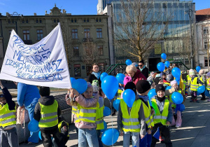 Dzieci maszerują trzymając niebieskie balony.