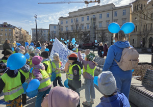 Dzieci maszerują trzymając niebieskie balony.