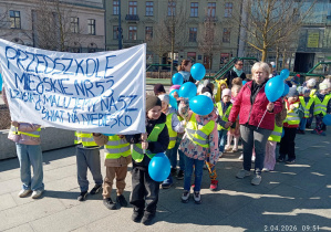 Dzieci maszerują trzymając niebieskie balony.