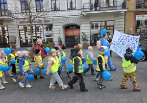 Dzieci maszerują trzymając niebieskie balony.