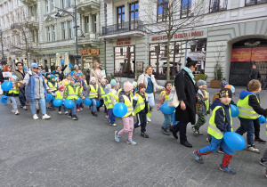 Dzieci maszerują trzymając niebieskie balony.