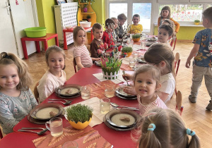Dzieci jedzą obiad przy udekorowanych stolikach w przedszkolu.