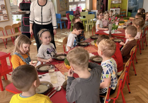 Dzieci jedzą obiad przy udekorowanych stolikach w przedszkolu.