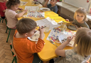 Dzieci jedzą obiad przy udekorowanych stolikach w przedszkolu.