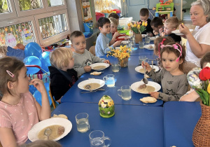 Dzieci jedzą obiad przy udekorowanych stolikach w przedszkolu.