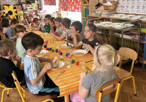 Dzieci jedzą obiad przy udekorowanych stolikach w przedszkolu.