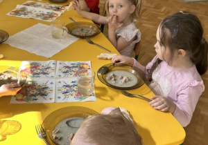 Dzieci jedzą obiad przy udekorowanych stolikach w przedszkolu.