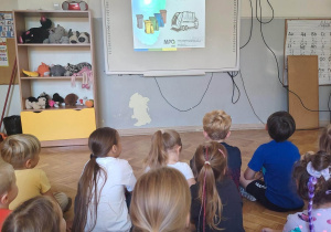 Dzieci oglądają prezentację " Jak dbać o planetę" wyświetlaną na ekranie.