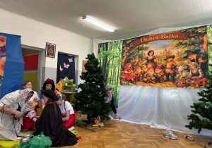 Na scenie aktorzy - Kopciuszek, Kot w butach, Śnieżka, Czerwony Kapturek i Koziołek Matołek za choinka skrywa się Wilk